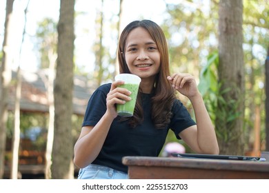 Asian women are happy to sit and work in a coffee shop. There are green trees surrounded by nature. Business planning is a good idea. - Shutterstock ID 2255152703