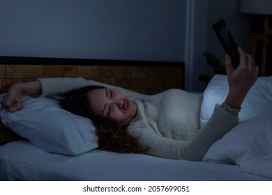 Asian Women Lie Down To Sleep, Cover Up With Blankets, Turn Off The Lights, Hold Their Smartphones And Play Games Before Bedtime In Their Bedroom At Home. 