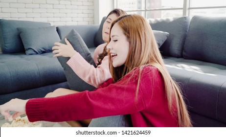 Asian Women Playing Pillow Fight And Eating Popcorn In Living Room At Home, Group Of Roommate Friend Enjoy Funny Moment While Lying On The Sofa. Lifestyle Women Relax At Home Concept.  