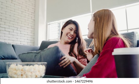 Asian Women Playing Pillow Fight And Eating Popcorn In Living Room At Home, Group Of Roommate Friend Enjoy Funny Moment While Lying On The Sofa. Lifestyle Women Relax At Home Concept.  