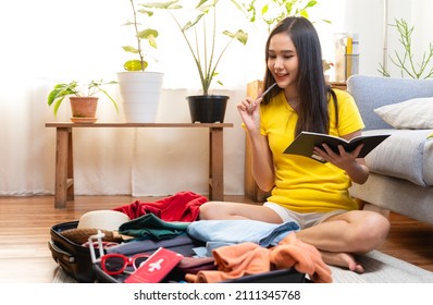 Asian women are preparing clothes in suitcases. She's choosing clothes, travel documents, itinerary for a solo trip, and checking the checklist in her living room in travel holiday concept - Shutterstock ID 2111345768