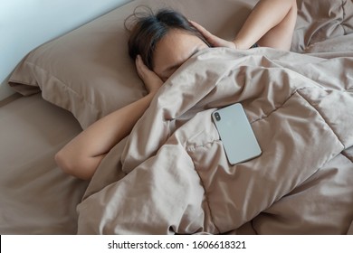 Asian women put their hands on their ears and don't want to wake up after hearing the alarm clock from their mobile phone.