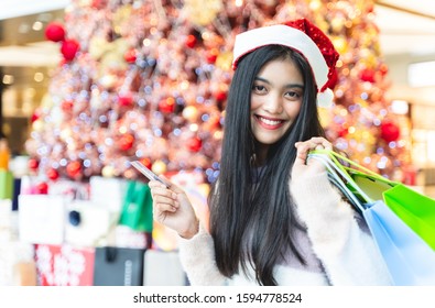 Asian Women Are Shopping In The Winter And Sale Season In The Hands Are Holding Credit Cards And Shopping Bags And Smiling With The Blur Chrismas Tree Background In Shopping And Travel Concept