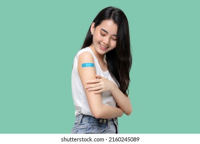 Asian Women Show Bandage On Arm. Happy Asian Woman Feels Good After Received Vaccine Isolated On Green Background.