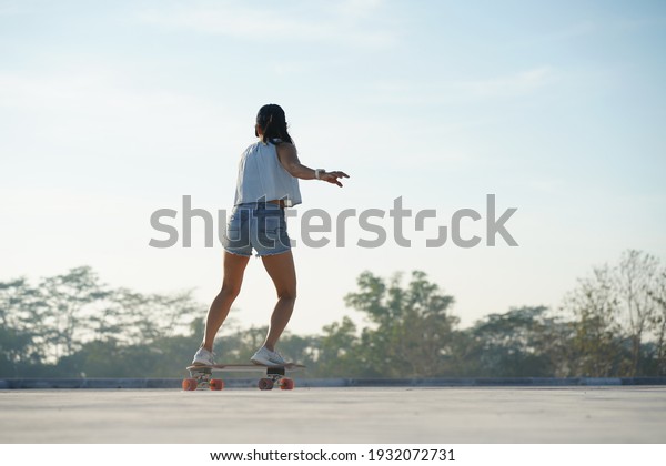 Asian women surf skate or skates board outdoors on\
beautiful summer day. Happy young women play surf skate at park on\
morning time.