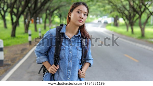 Asian\
women tourists and backpackers waiting car and Freedom traveler\
woman standing with raised arms at the\
roadside.