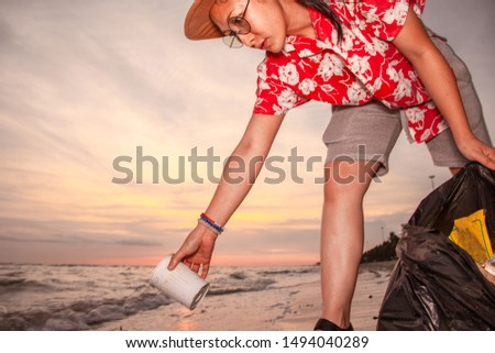 Asian women tourists picking up plastic garbage cleaning on the beach During the sunset . Tourists volunteers are helping to collect garbage picking up trash .  Cleaning environmental pollution 
