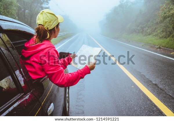 Asian women\
travel relax in the holiday. Traveling by car park. View map for\
Nature tours during the rainy\
season.