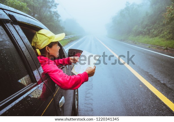 Asian women\
travel relax in the holiday. Traveling by car park. View map for\
Nature tours during the rainy\
season.