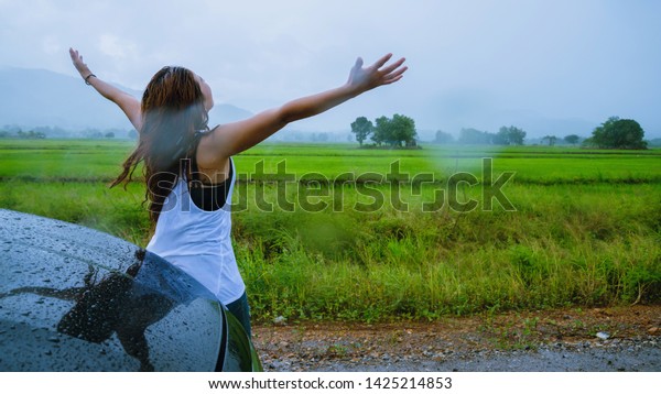 Asian women travel relax in the holiday.The\
girl smiled happy and enjoyed the rain that was falling. Tourist\
travelling driving in the countryside during the rainy season,\
Green rice fields,\
Thailand.