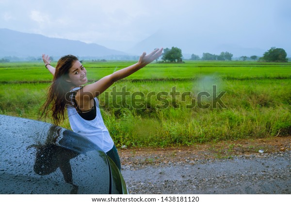 Asian women travel relax in the holiday.The\
girl smiled happy and enjoyed the rain that was falling. Tourist\
travelling driving in the countryside during the rainy season,\
Green rice fields,\
Thailand.