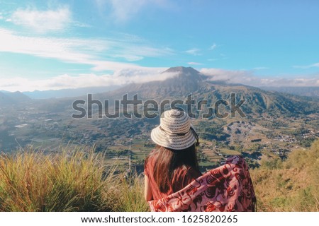 Asian women traveller standing behind looking Batur Mountain from Pinggan village which located in Kintamani Bangli, Bali, Indonesia.
