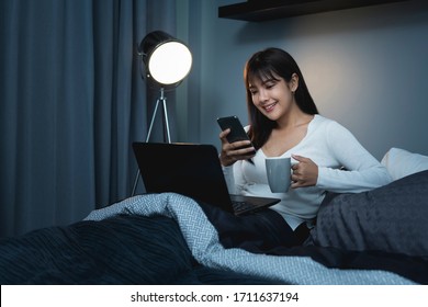 Asian Women Using The Smart Phone And Working On Laptop On The Bed Before She Sleeping At Night.