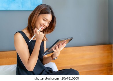 Asian women using tablet and stylus for drawing in bed at home. A smiling face represents successful confident. digital draws on a graphic screen, young woman artist or designer.
