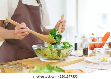 Asian women using wooden spoon to mixing ingredients and slices of fresh vegetable in the glass bowl to cooking breakfast meal and vegetable salad while making homemade healthy food lifestyle in home. - Powered by Shutterstock