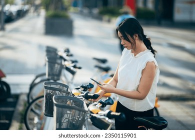 Asian women are utilizing their smartphones to rent shared bicycles for their daily commutes. With a few taps on their screens, they unlock the bikes and set off on their eco-friendly journey. - Powered by Shutterstock