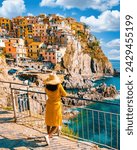 Asian women visiting Manarola in Cinque Terre Italy,beautiful colorful town of La Spezia Liguria one of the five Cinque Terre, woman with hat standing by the ocean during summer in Europe