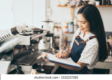 Asian women waiter hands on notebook, taking customer orders in restaurant or cafeteria, Thai girl coffee shop worker wearing apron write order serving for a client, writing food list service concept