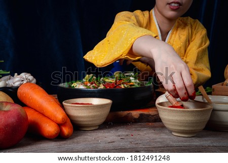Asian women wearing Korean traditional costumes (hanbok) are mixing fresh stir-fry and kimchi ingredients with ingredients such as salt, garlic, gochugaru, fresh vegetables.