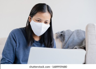  Asian women wearing a protection mask epidemic of flu or covid-19 in the living room at home. Asia woman using a laptop and work from home. Health and illness concept