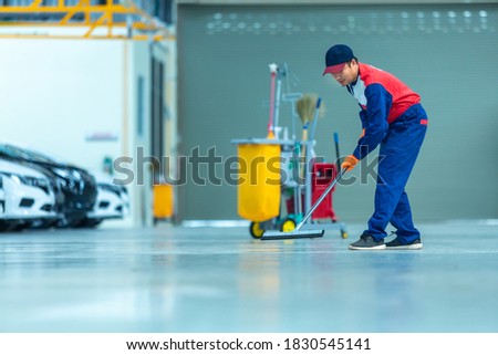 Asian worker in car mechanic repair service center cleaning using mops to roll water from the epoxy floor. Mops in the car repair service center.