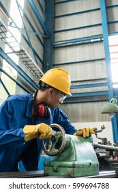 Asian Worker Checking Quality Behind An Industrial Machine Indoors In The Factory