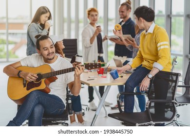 Asian Worker Playing The Guitar Over The Group Of Asian And Multiethnic Business People With Casual Suit Talking And Eatting With Happy Action When Lunch Time In The Creative Office Workplace
