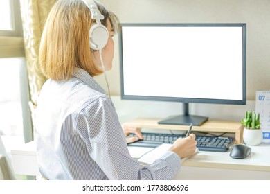 Asian Working Woman Wear Headphone And Looking To Monitor Computer With Blank Screen At Her Home. Work From Home Concept. 