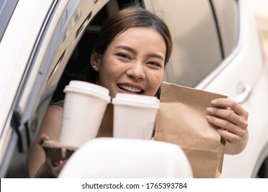 Asian Young adult in car holding disposable bag and coffee tray for take out food from drive thru service restaurant. Drive thru is new normal and popular service after coronavirus covid-19 pandemic.