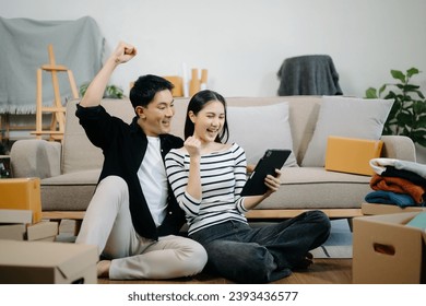 Asian young attractive couple man and woman use tablet and smartphone online shopping furniture decorate house with carton package move in new house. Young married asian moving home. 

 - Powered by Shutterstock