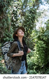 Asian young beautiful female backpacker traveling alone in forest wild. Attractive girl traveler look around and explore while walk in nature wood with happiness and fun during holiday vacation trip.