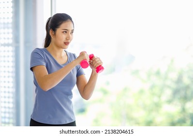 Asian young beautiful happy healthy female athlete sport girl in casual sporty outfit standing smiling holding small pink dumbbells in hands guarding learning practicing boxing exercise in classroom.