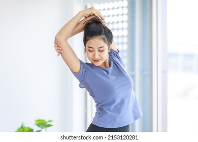 Asian young beautiful happy healthy female sport girl in casual sporty outfit standing smiling holding hand up stretching arm and body exercising training routine yoga pilates practice in living room. - Powered by Shutterstock