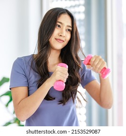 Asian young beautiful happy healthy female athlete sport girl in casual sporty outfit standing smiling holding small pink dumbbells in hands guarding learning practicing boxing exercise in classroom.