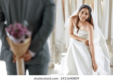 Asian young beautiful happy long hair bride in white wedding dress with seethrough lace veil sit smile waiting for groom in gray suit who hide flower bouquet behind back to surprise in dressing room. - Powered by Shutterstock