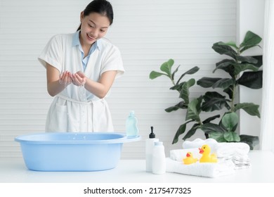 Asian young beautiful mother wear bathrobe is touching water with her hands to find the suitable temperature for bathing her newborn baby at home. Child care bathing concept - Powered by Shutterstock