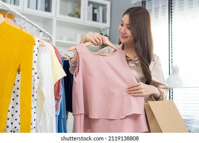 Asian Young Beautiful Woman Look Products Of Clothes In Shopping Mall. Attractive Happy Girl Enjoy Walking In Department Store To Choose Dress And New T-shirt From Clothing Racks In Marketplace Center