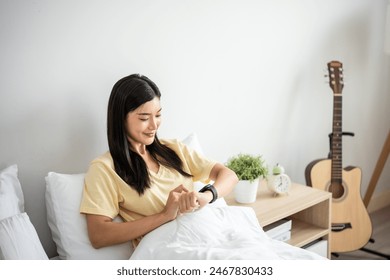 Asian young beautiful woman looking on smartwatch checking sleep rate. Attractive girl get up from sleep on bed in morning then using application technology collect data on device in bedroom at home. - Powered by Shutterstock