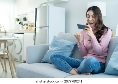 Asian Young Beautiful Woman Playing Mobile Game On Smartphone At Home. Attractive Casual Girl Feel Happy And Relax, Sit On Sofa Having Fun Touching Screen On Phone To Play Video Enjoy Victory In House