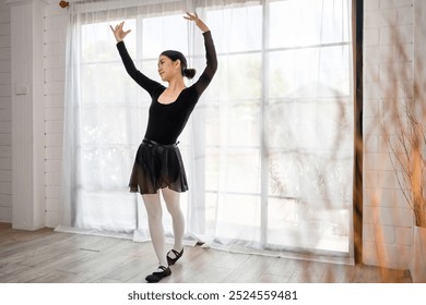 Asian young beautiful woman practice dancing ballet rehearsing at home. Attractive young girl ballet dancer spinning and jumping in a tutu and pointe shoes, doing stretching dance with yoga elements. - Powered by Shutterstock