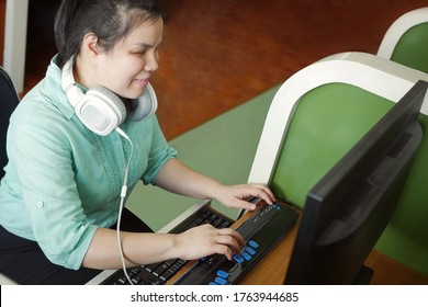 Asian young blind person woman with headphone using computer with refreshable braille display or braille terminal a technology device for persons with visual disabilities.