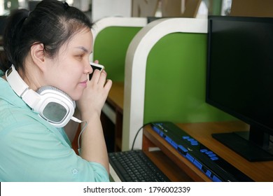 Asian Young Blind Person Woman With Headphone Using Smart Phone With Voice Assistive Technology For Disabilities Persons In Workplace With Computer And Braille Display On Table.