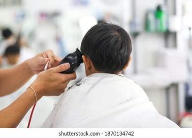 An Asian young boy getting a haircut at a barber shop. 