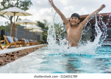 Asian Young Boy Having A Good Time In Swimming Pool, He Jumping And Playing A Water In Summer.