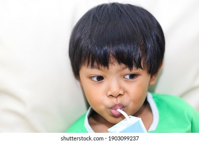 An Asian Young Boy Holding And Drinking A Carton Of Milk. 