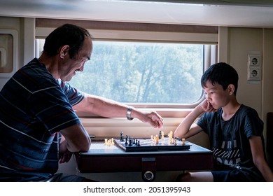 Asian Young Boy Playing Chess With His Grandfather At Train.