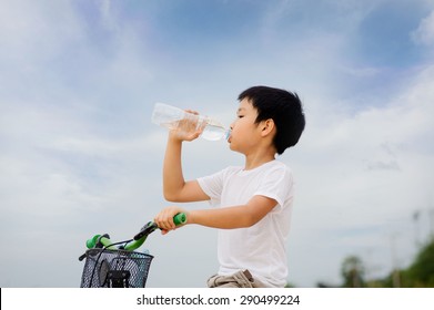 Asian Young Boy Sit On Bicycle  Drinking Fresh Water From Plastic Bottle After Sport In Daylight