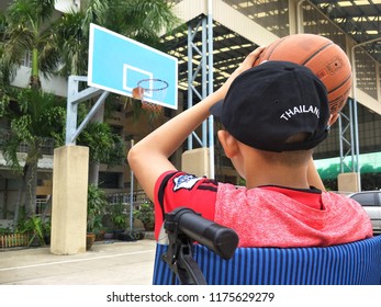 Asian Young Boy In Wheelchair Is Trying To Practice Basketball After Convalesce From Torn Ankle Ligament In Basketball Court At School, Tha Cha Lom, Samutsakhon, Thailand, 09092018