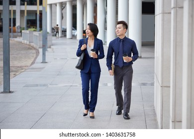 Asian Young Business Partners Walking In The City Together Talking And Drinking Coffee From Disposable Cups