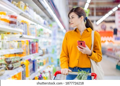 Asian Young Business Woman Is Searching Information Of Products By Smart Phone At Grocery Store